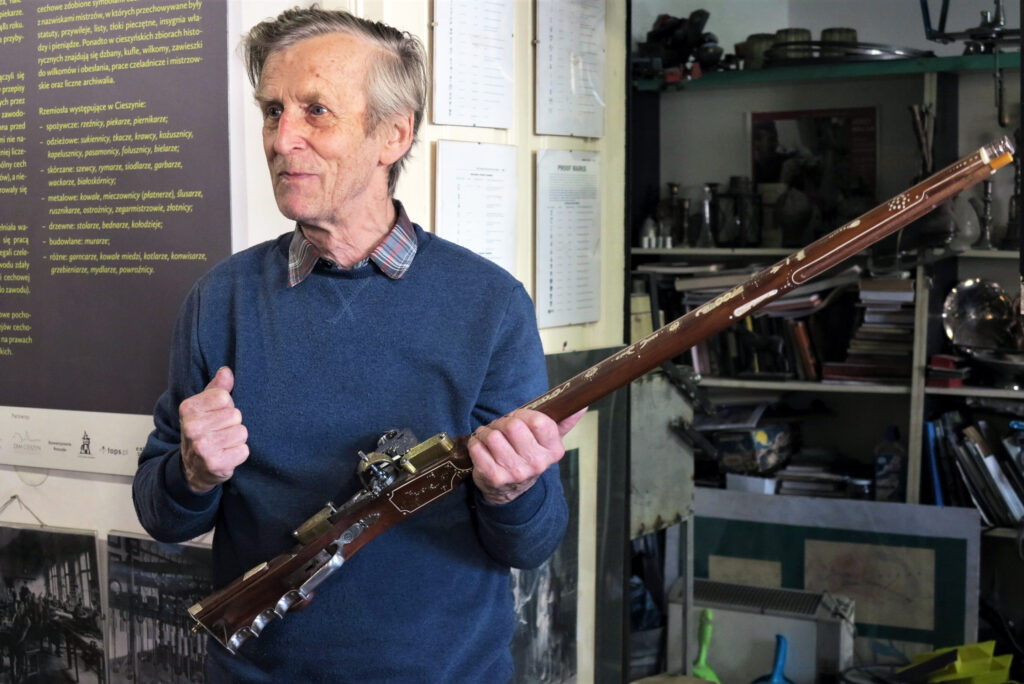 Rusznikarz, mężczyzna w średnim wieku, pokazuje zabytkową, długą broń palną.