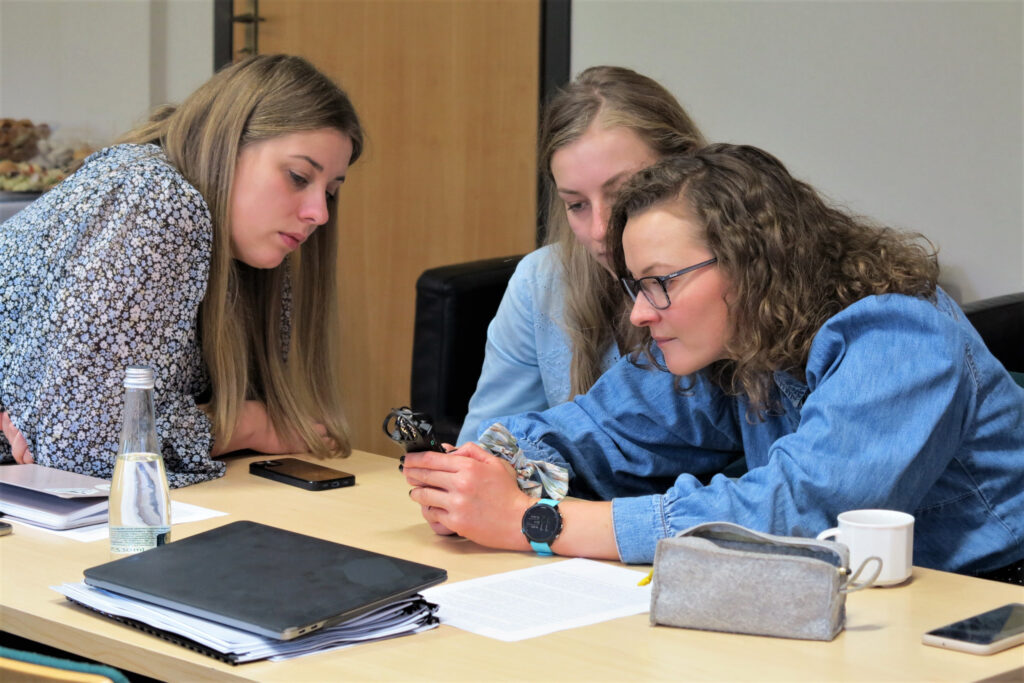 Trzy młode kobiety pracują przy stole na warsztatach z historii mówionej.