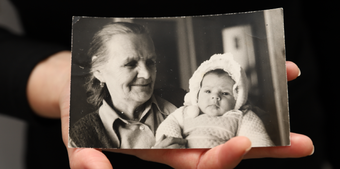 zdjęcie przedstawiające dłoń, która trzyma zdjęcie archiwalne - starszą kobietę trzymającą niemowlę